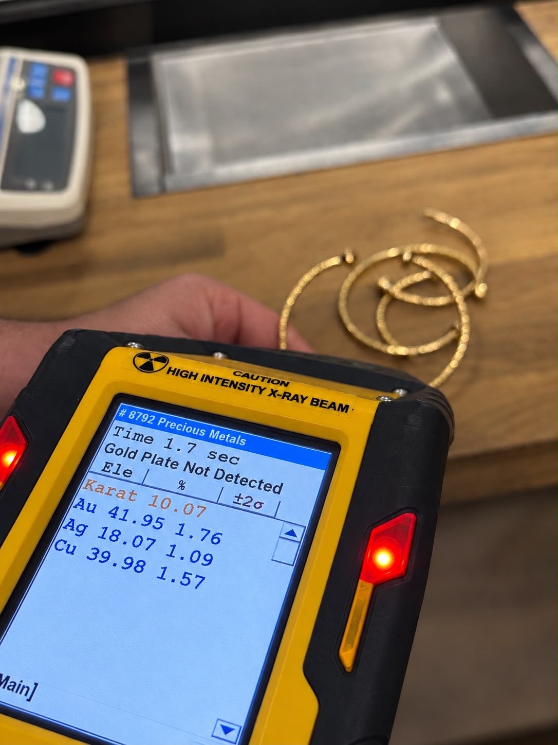 The XRF gun showing a precious metals reading: 10.07 karat, with gold, silver and copper percentages on screen
